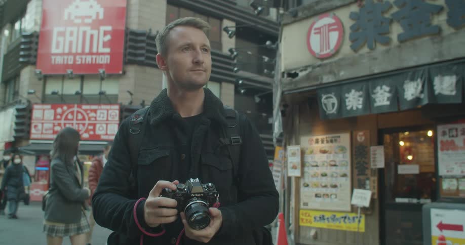 A white man stands in a street in an asian city and takes a photograph