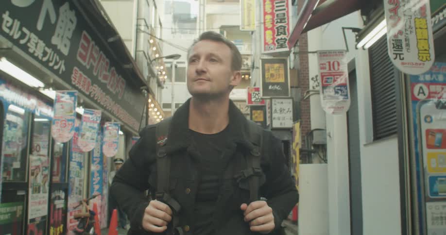 A caucasian man walks through an asian town of small stores