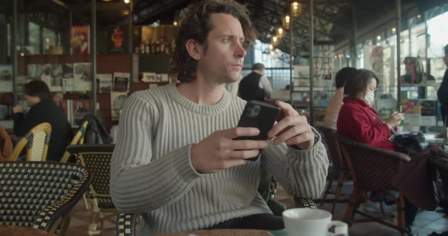 A man sitting in a restaurant looks around and uses his cell phone