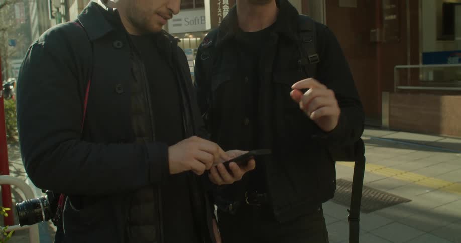 Two friends stand and use a smartphone to find the location where they wanna go to