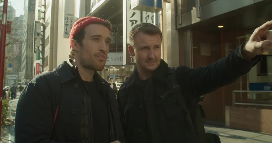 Two men standing in the street talking and looking at a smart phone