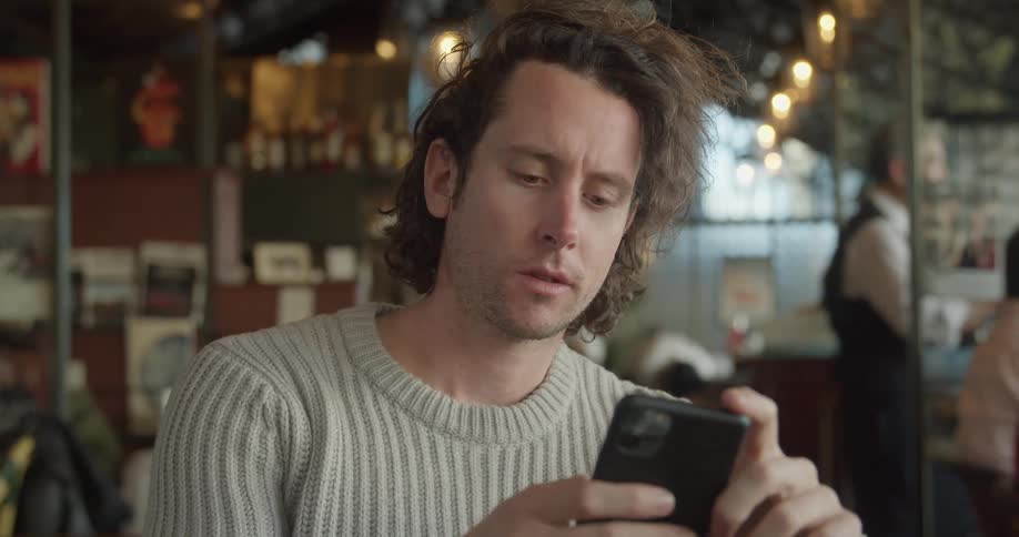 Man sitting at the table uses smartphone and smirks in a cafe