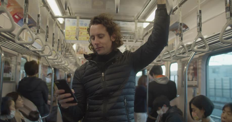 A man stands in the middle of a packed train car and uses his smart phone
