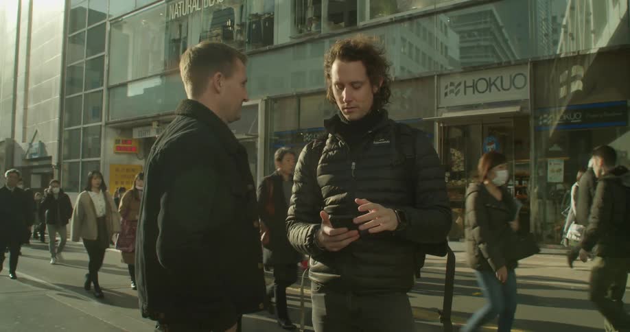 Two men standing in the street and talking while one holds a smart phone in his hand
