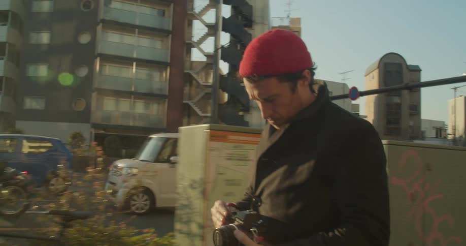 Man walks parallel to stopped street traffic adjusting camera