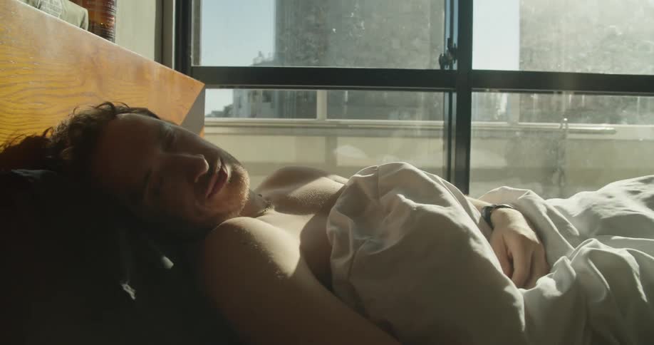 Man wakes up and checks his smartphone while the sun shines through the window