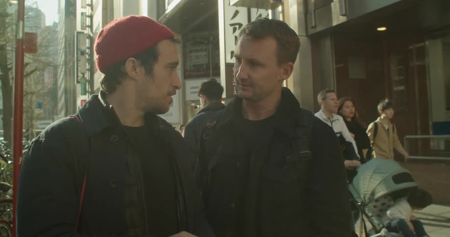 Two white males have a discussion on a busy city sidewalk