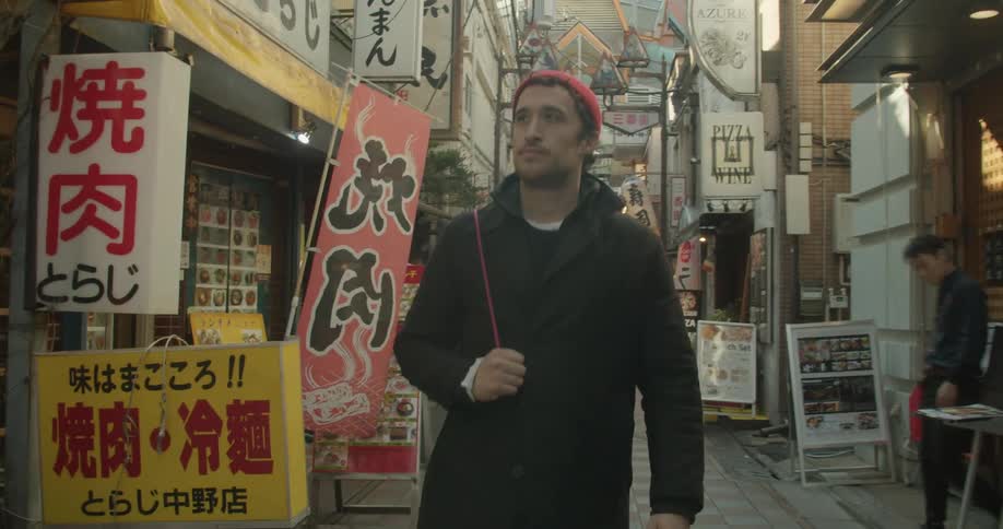 Man wearing a jacket and a beanie walks through an oriental market on a sunny day