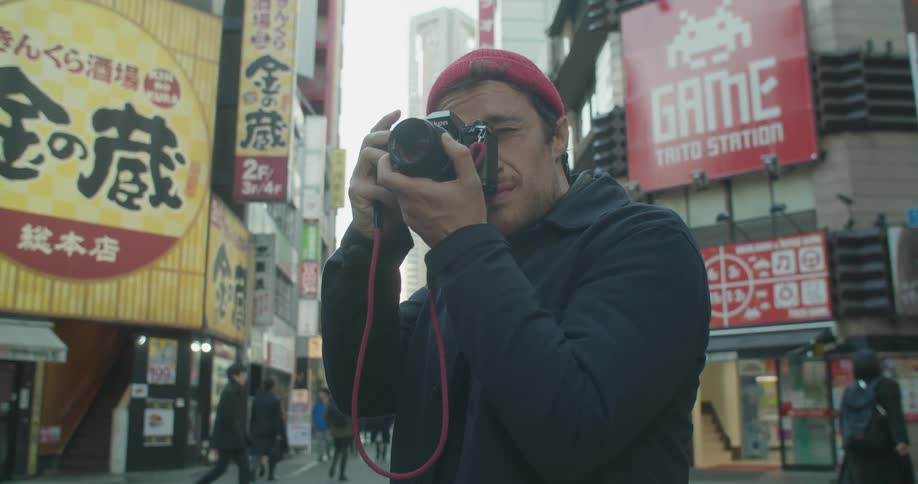 A man on the streets with a camera taking pictures with people and buildings in the background