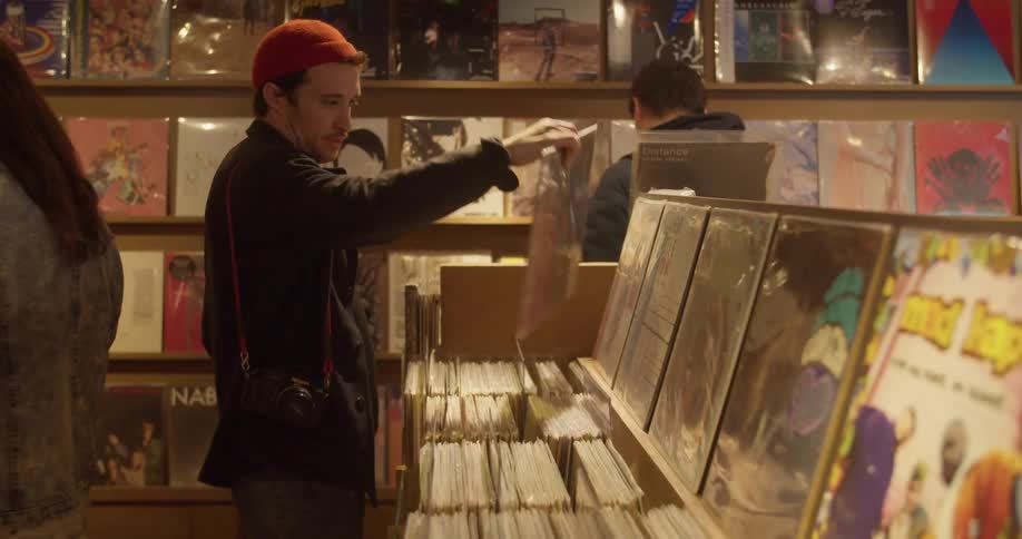 Person carrying camera and skateboard browses in record store