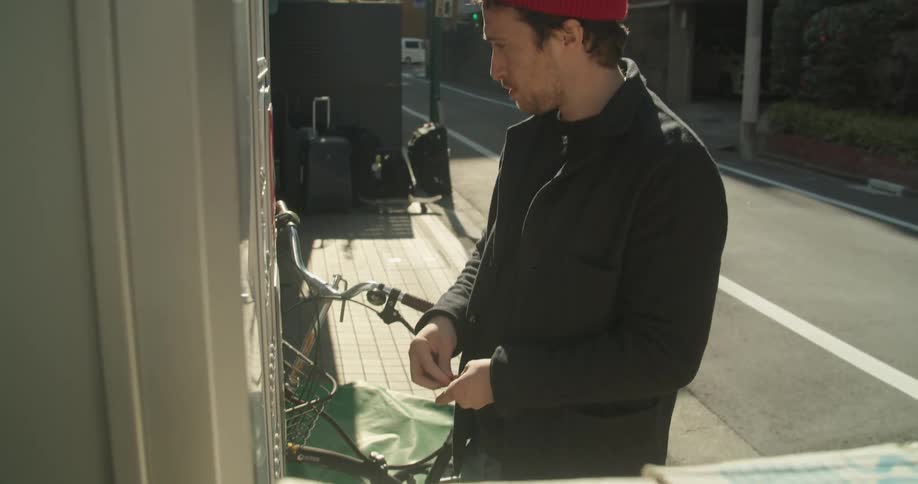 A man in the street putting money into a vending machine then hitting it