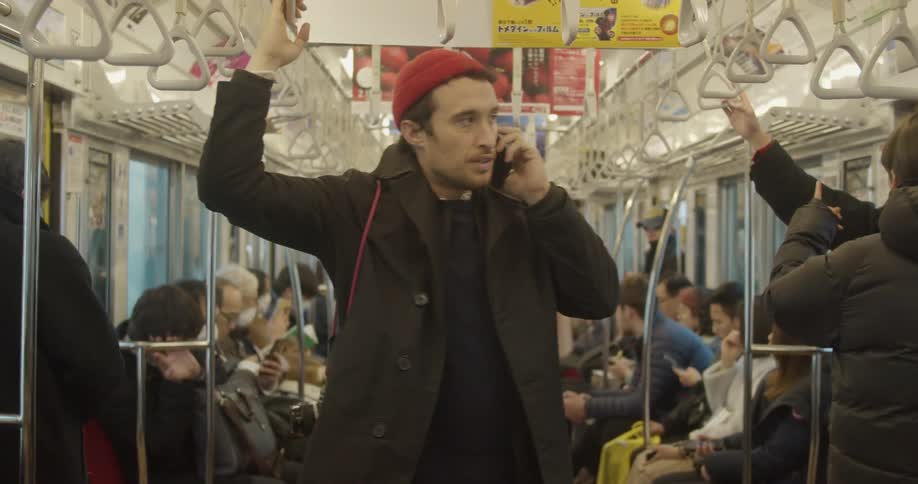 A man stands on a crowded subway and talks on his phone