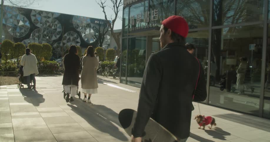Man carries a skateboard as he walks down a city street full of pedestrians
