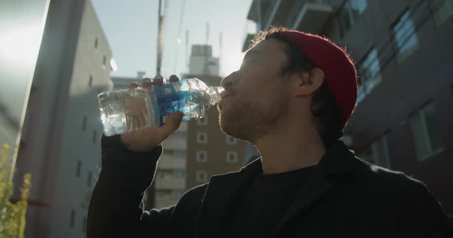 A man stands in a neighborhood street and drinks a bottle of water
