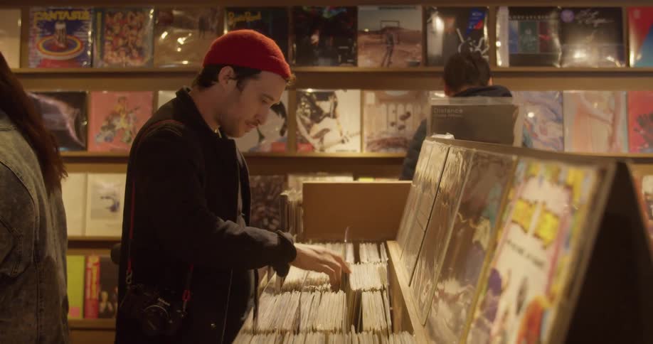A man with a camera slung over his shoulder flips through the albums in a record store