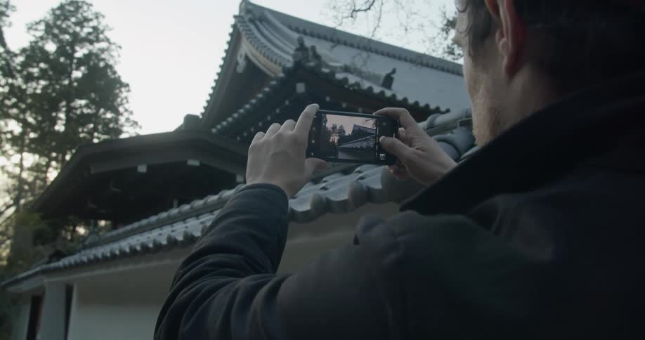 A man uses his smart phone to take a photo of a building with asian style architecture