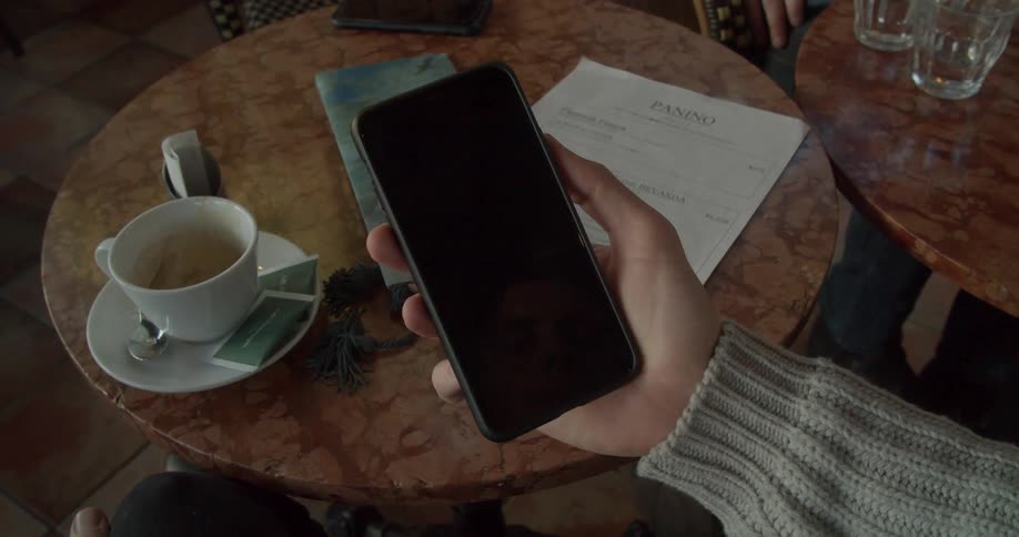 A man sits at a table in a cafe and holds his phone