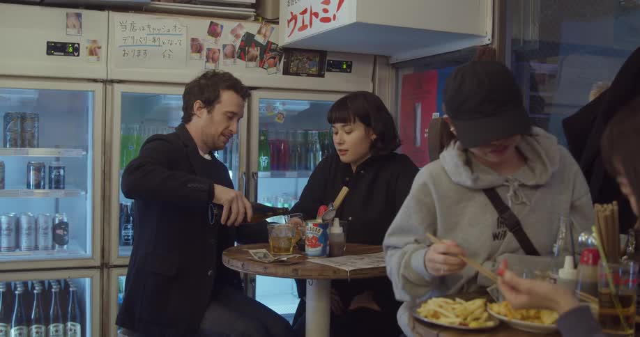 A man sitting with a woman at a small table in a restaurant pouring a drink