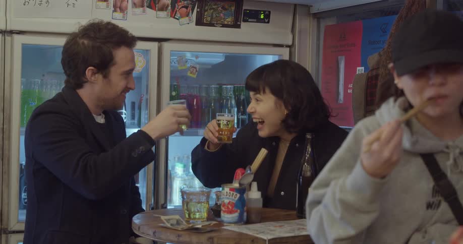 A man and woman at a restaurant toast their glasses together and drink as a woman at another table eats