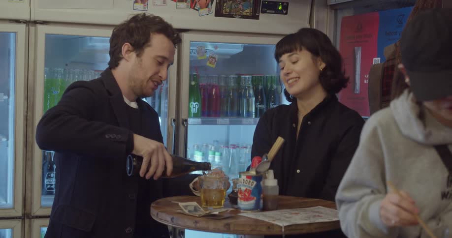 A man and woman sit at a table as he pours a drink