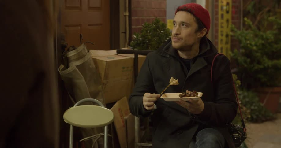 A man is sitting in a chair eating food from a skewer