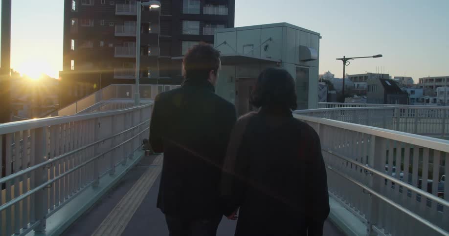 Couple holding hands walks across a bridge at sunset