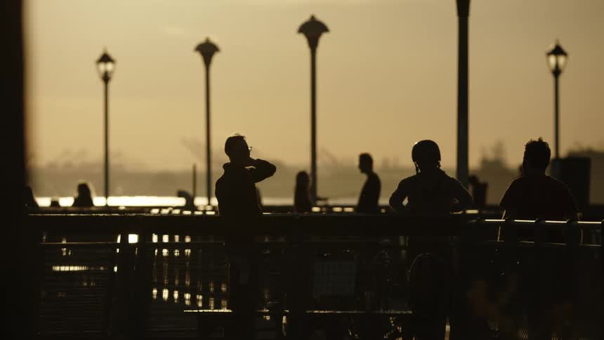 Groups of people hang out on a waterfront patio as a ferry passes by