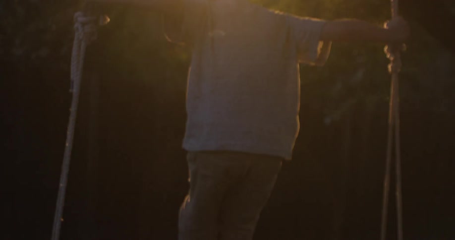 A boy stands on a large swing holding the ropes