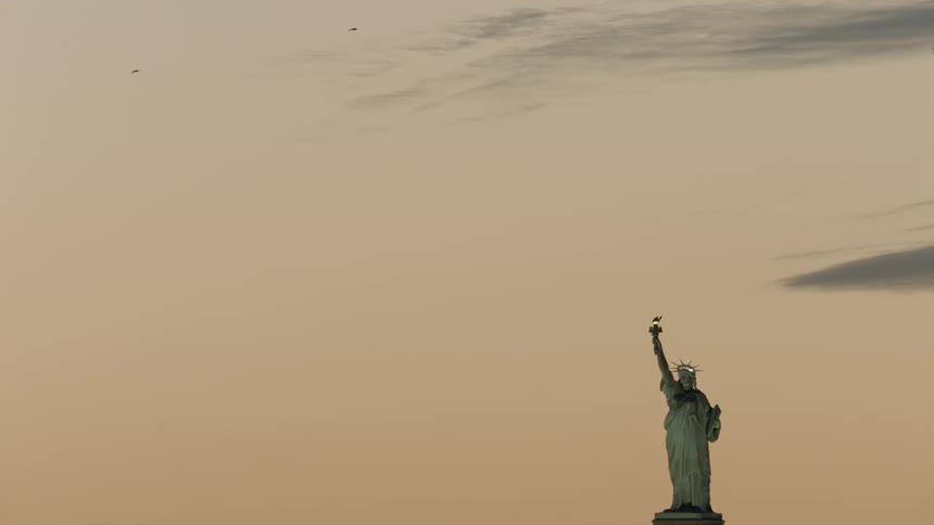 Birds fly over the statue of liberty at sunrise