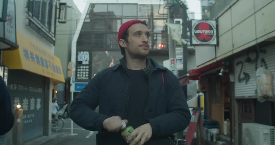 Man drinks from a water bottle as he walks near the stores and carries a camera