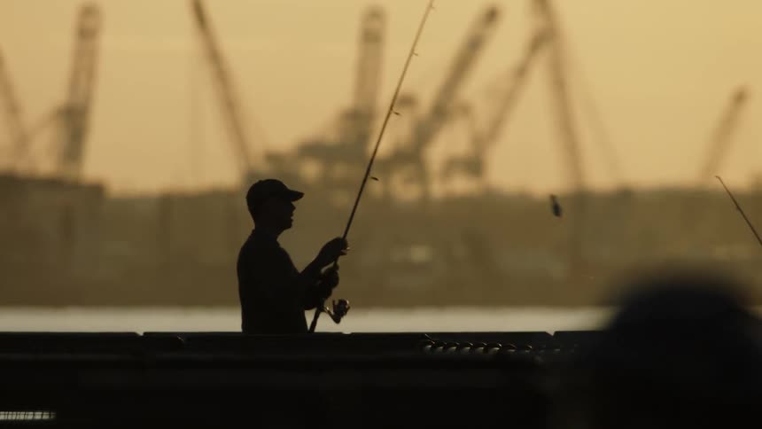 A man in front of the water picks up his fishing rod