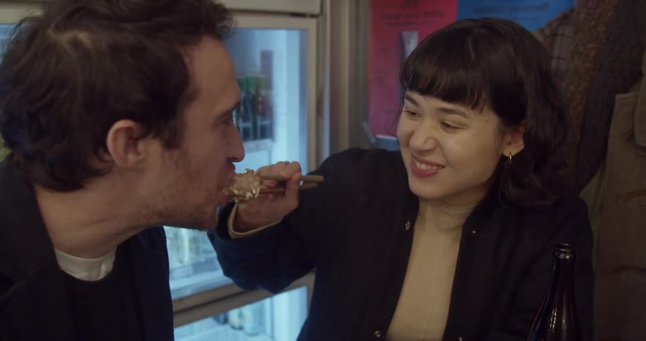 A woman feeds her boyfriend using chopsticks at a restaurant