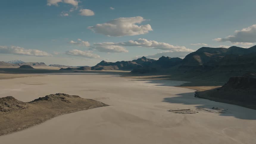 A aerial view of a flat desert next to a mountain range