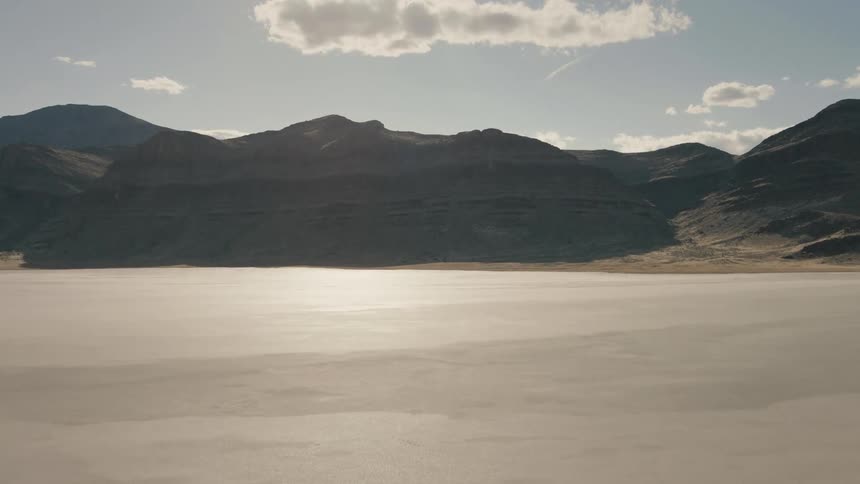 A flat barren landscape cracked from dryness near a mountain in a desert