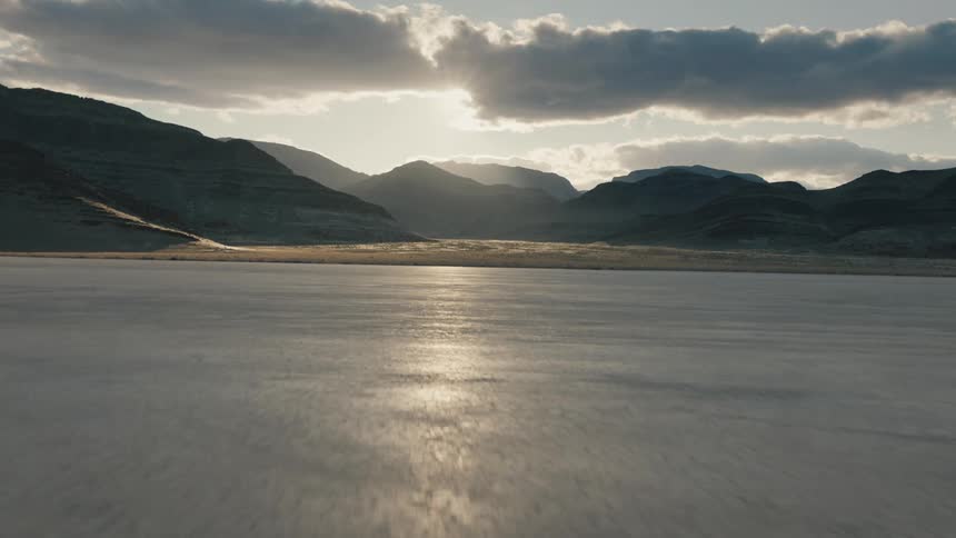 Sun shines behind clouds over mountains and dry desert earth