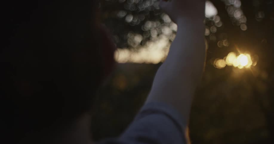 A boy reaches his hand into the sky as the sun sets