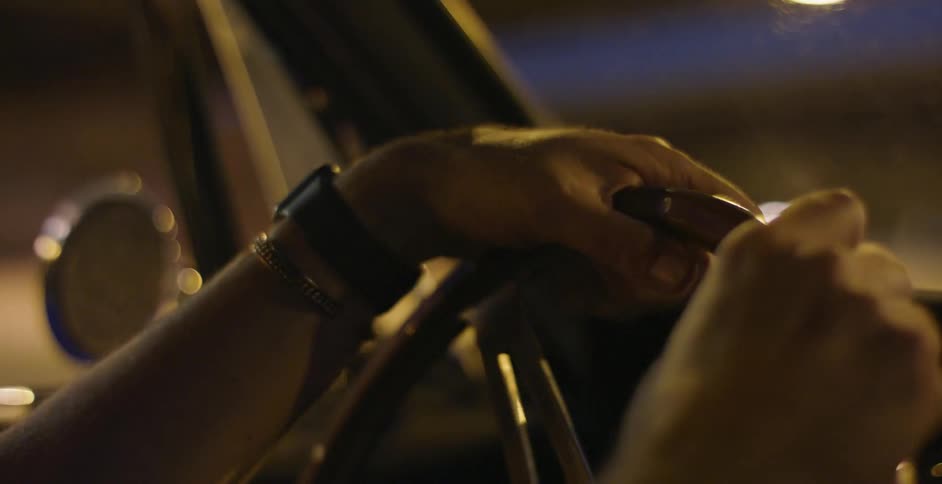 Hands relaxing on top of an old steering wheel while driving at night