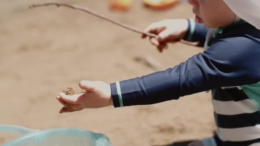Child holds stick and lets sand fall into bucket