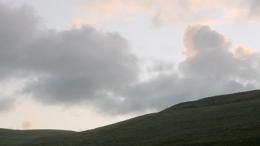 The sun hides behind clouds above grassy hills