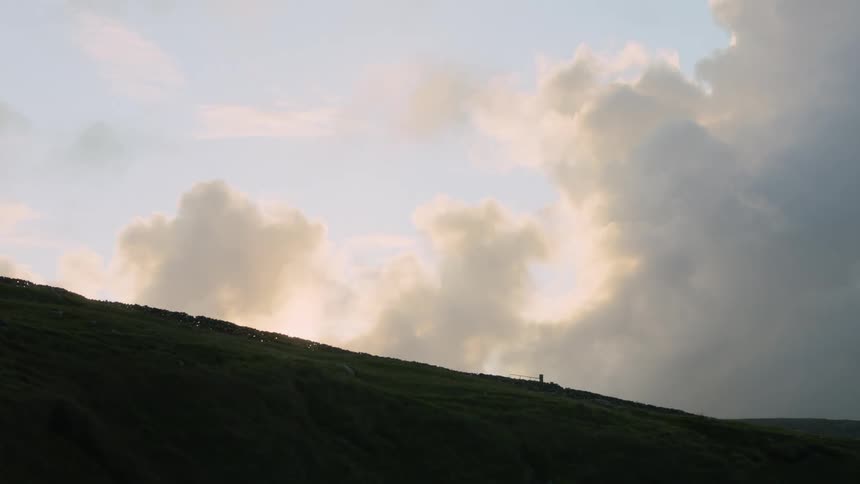 A hill with the sky and clouds in the background