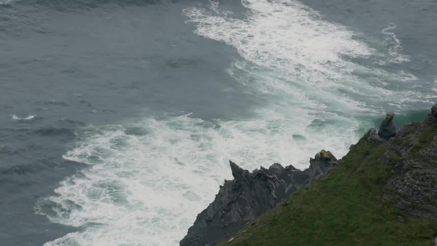 Waves crash onto a rocky moss filled cliff