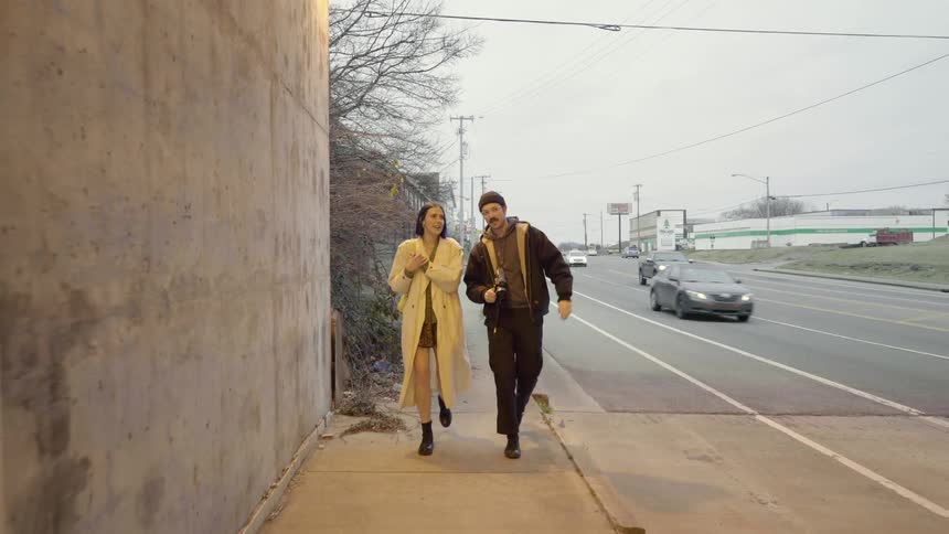 Man and woman walk on a sidewalk as cars pass by