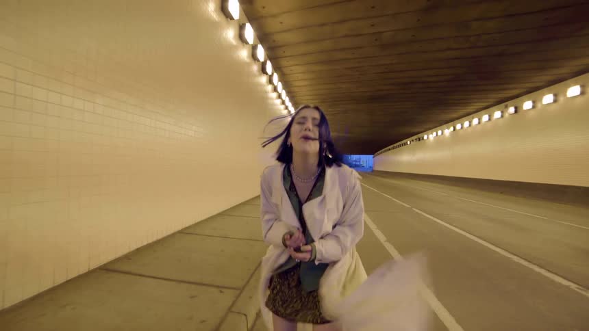 A woman walks through an empty tunnel singing for a music video