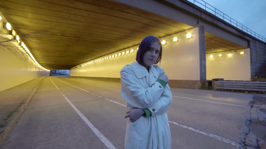 A teenager stands in a road as she hugs herself