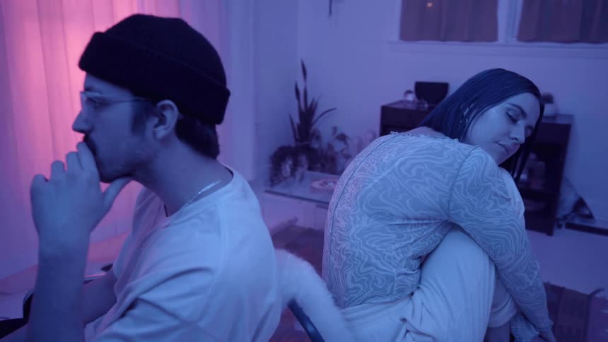 Man and woman sitting back to back in chairs in a blue lit room