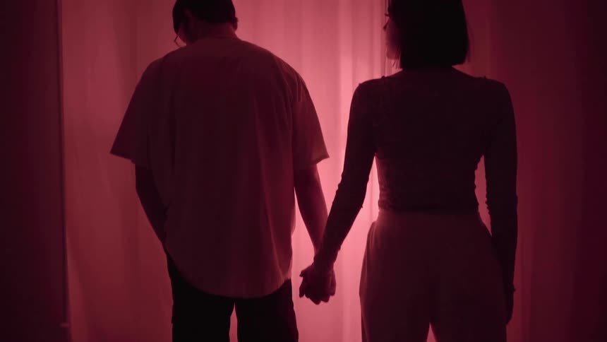 A man and a woman hold hands while standing in a living room