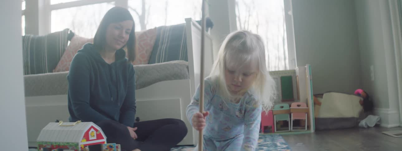 A toddler girl uses a toy broom and dust pan to clean up