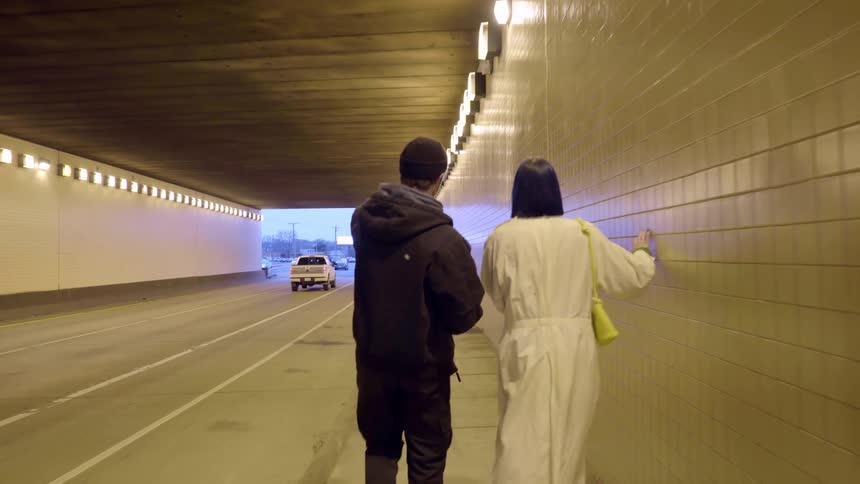 Two people are walking in a tunnel as cars drive by