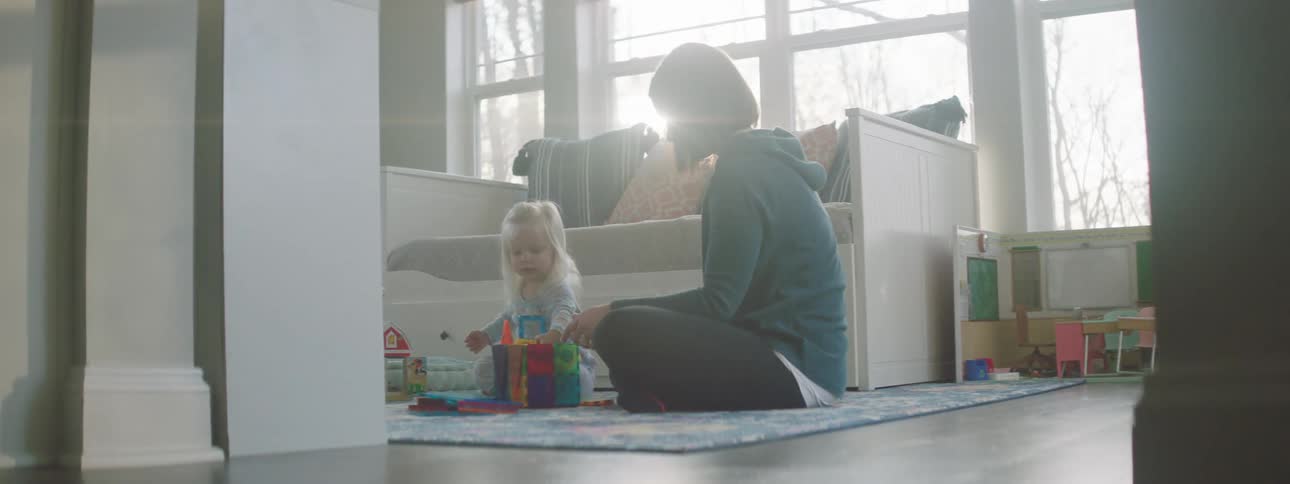 A little girl plays as her mother sits and watches her