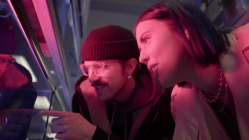 Man and woman touch a fish tank in a red lit room